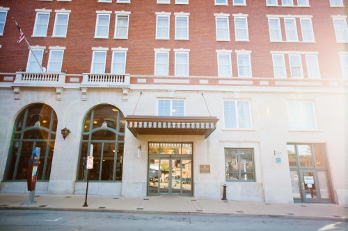 Historic brick building with large windows and an entrance, featuring a canopy and decorative architectural details.