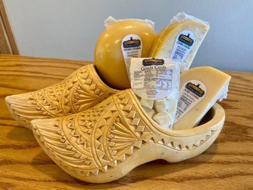 Two wooden clogs filled with various types of Gouda cheese and a round cheese ball on a wooden surface.