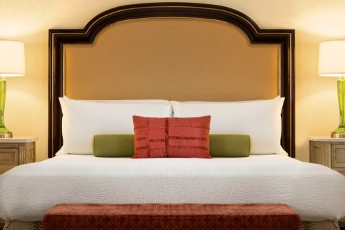 A neatly made bed with decorative pillows, a stylish headboard, and bedside lamps in a warm-toned hotel room.