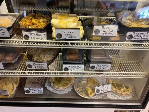 A display case filled with various prepared meals, including burritos, lasagna, and ratatouille, with price labels.