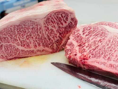 Close-up of marbled beef on a cutting board, showcasing intricate fat patterns and a sharp knife beside it.