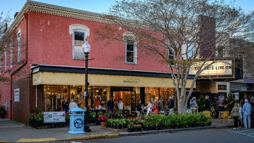 A vibrant street scene with a pink building, outdoor seating, and flower displays, bustling with people enjoying the atmosphere.