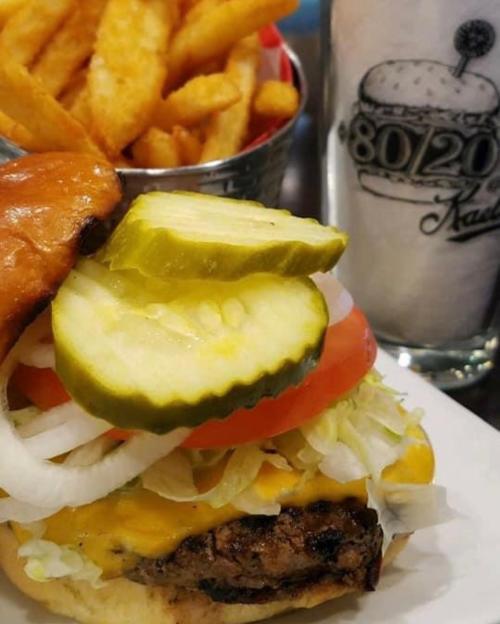 A juicy cheeseburger with pickles, lettuce, tomato, and onions, served with a side of crispy fries and a milkshake.