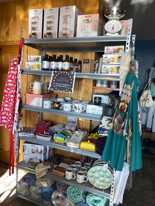 A display shelf filled with various kitchenware, towels, and holiday-themed items in a cozy shop setting.