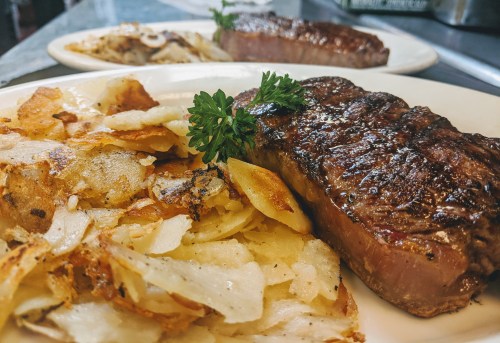A juicy steak garnished with parsley, served alongside crispy golden potato slices on a white plate.