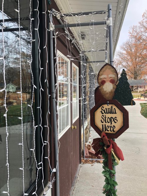 A festive sign reading "Santa Stops Here" next to a door, adorned with holiday lights and decorations.