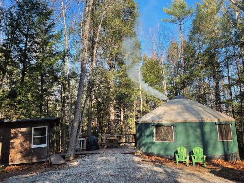 A green yurt surrounded by trees, with smoke rising from the chimney and two green chairs in front.