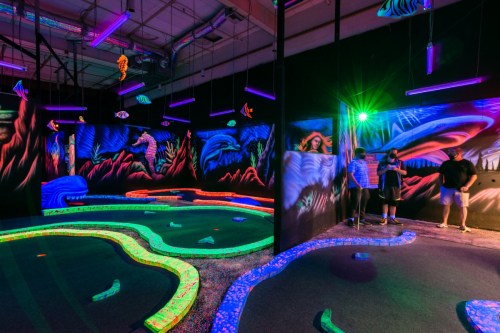 A vibrant glow-in-the-dark mini-golf course with colorful obstacles and neon decorations, featuring players enjoying the game.