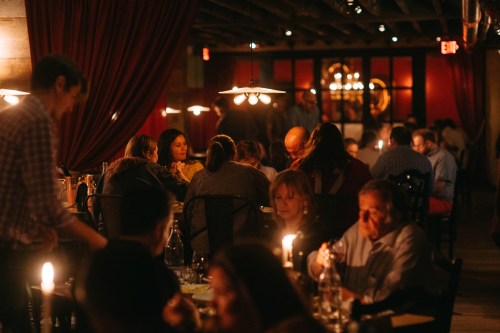 A dimly lit restaurant scene with people dining, chatting, and enjoying a cozy atmosphere with candlelight.