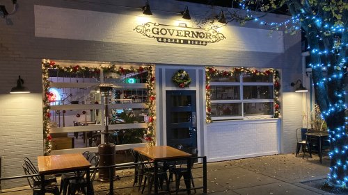 A festive restaurant exterior decorated with holiday lights and garlands, featuring outdoor seating.
