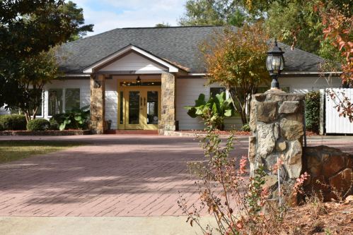 A charming house with a stone entrance, surrounded by greenery and a brick driveway, under a clear blue sky.
