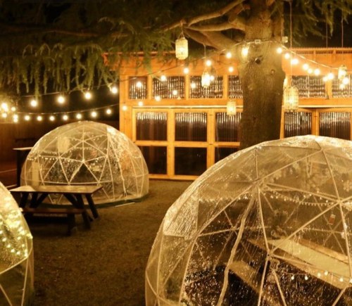 Cozy outdoor dining area with illuminated igloo-like structures and string lights under a tree at night.