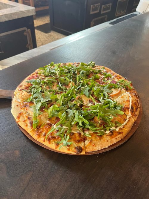 A freshly baked pizza topped with arugula on a wooden serving board, placed on a dark countertop.