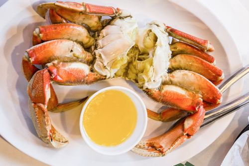 A cooked crab on a white plate, accompanied by a small bowl of yellow dipping sauce.