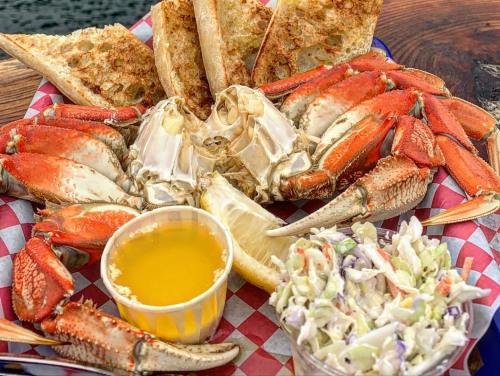 A plate of crab with melted butter, lemon, coleslaw, and toasted bread, served on a checkered paper.