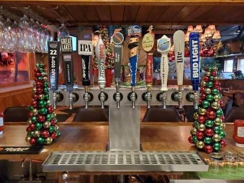 A bar with a row of beer taps and festive decorations made of red and green ornaments on either side.