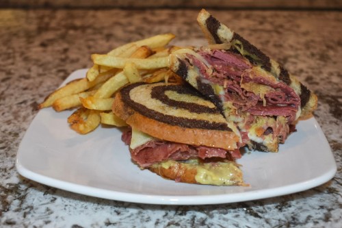 A plate with a sliced sandwich featuring layered meats and cheese, served with a side of golden French fries.