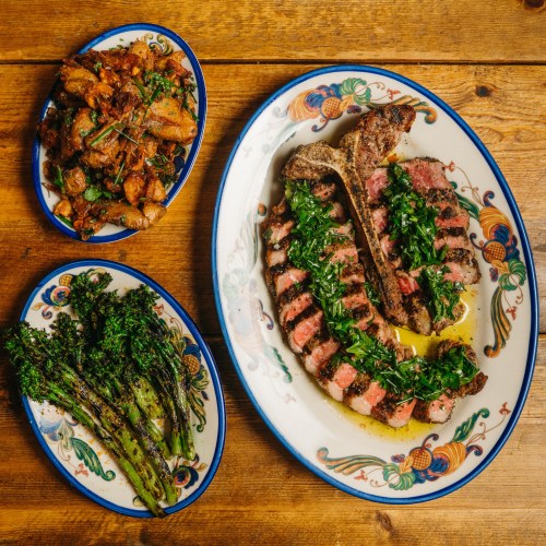 A beautifully plated meal featuring grilled steak with herbs, roasted potatoes, and sautéed asparagus on a wooden table.