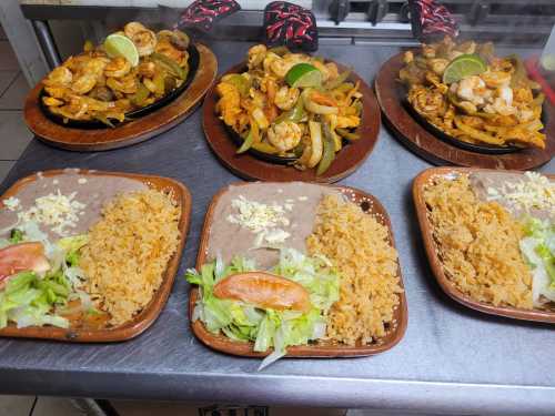 Plates of sizzling shrimp fajitas with rice, beans, and fresh vegetables, garnished with lime and served on wooden platters.