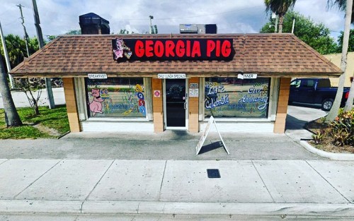 Exterior of Georgia Pig restaurant with a sign, colorful window art, and a sidewalk A-frame sign.