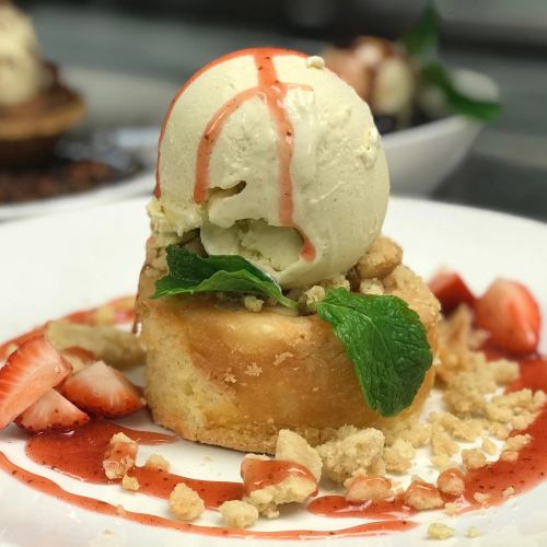 A dessert featuring a cake topped with vanilla ice cream, strawberry sauce, mint leaves, and fresh strawberry slices.