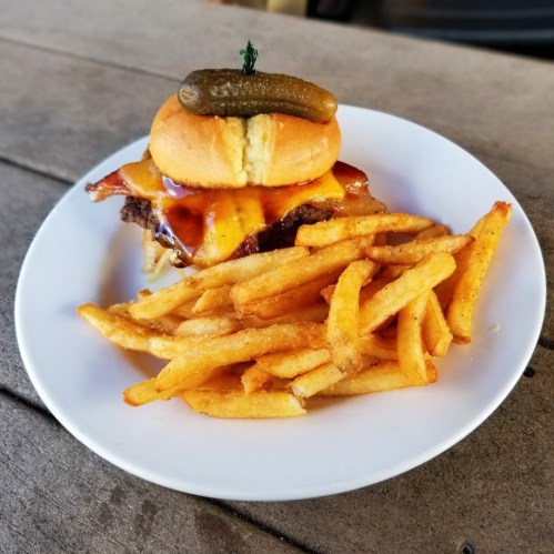 A juicy burger topped with a pickle and bacon, served with a side of crispy French fries on a white plate.