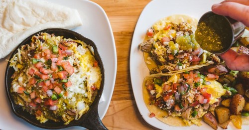 A skillet with cheesy nachos and two tacos topped with salsa, alongside a plate of seasoned potatoes.