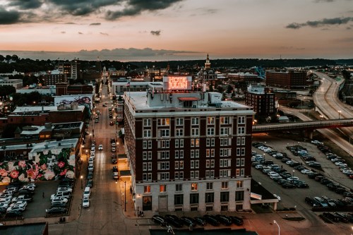 Aerial view of a city at sunset, featuring buildings, streets, and a prominent neon sign on a rooftop.