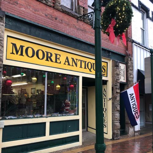 A storefront labeled "Moore Antiques" with festive decorations and a red, white, and blue flag hanging outside.