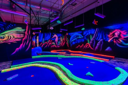 A vibrant glow-in-the-dark mini-golf course with colorful underwater murals and neon pathways.