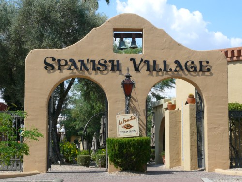 Entrance to Spanish Village, featuring an archway with the name and decorative elements, surrounded by greenery.
