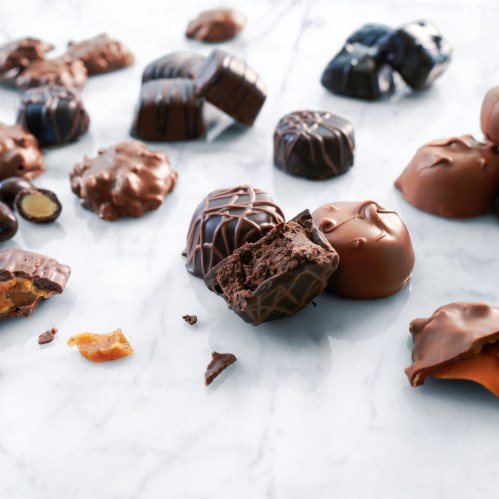 An assortment of chocolate candies, some whole and others cut open, revealing their fillings, on a marble surface.