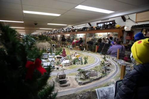 A model train display with a winding track, surrounded by spectators in a well-lit room.