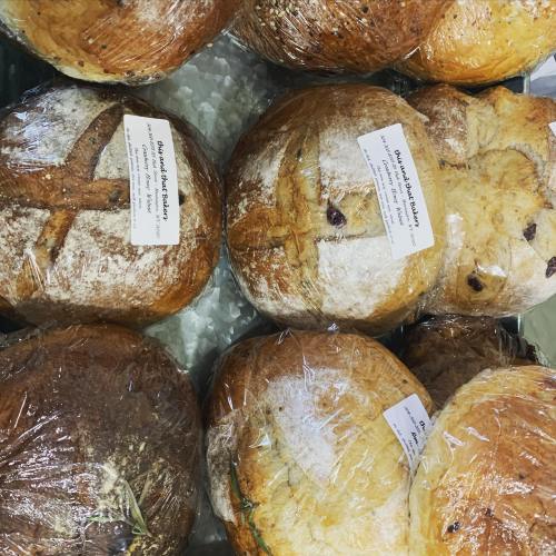 A variety of freshly baked bread loaves wrapped in plastic, labeled with names and prices.