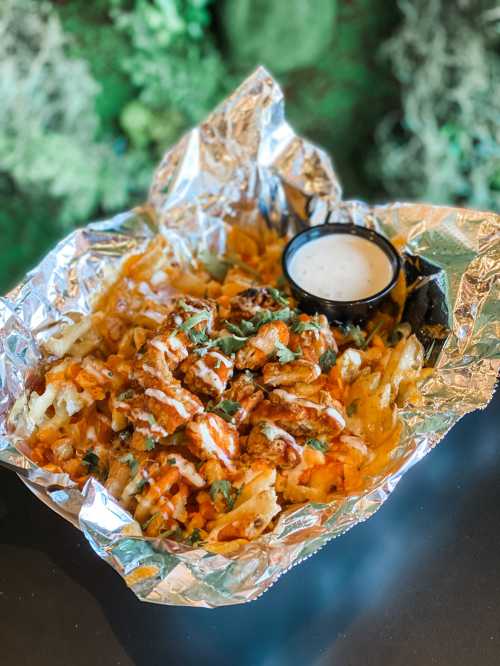 A foil tray filled with loaded fries topped with chicken, drizzled sauce, and a side of ranch dressing.