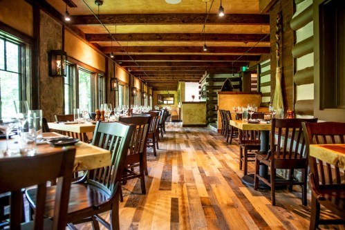 Interior of a rustic restaurant featuring wooden tables, chairs, and a warm, inviting atmosphere with natural light.