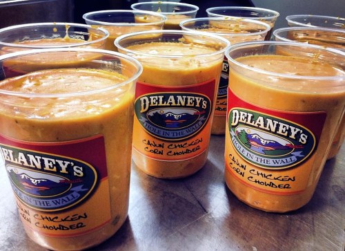 Cups of Delaney's Cajun Chicken Corn Chowder lined up on a counter, showcasing a creamy orange soup.