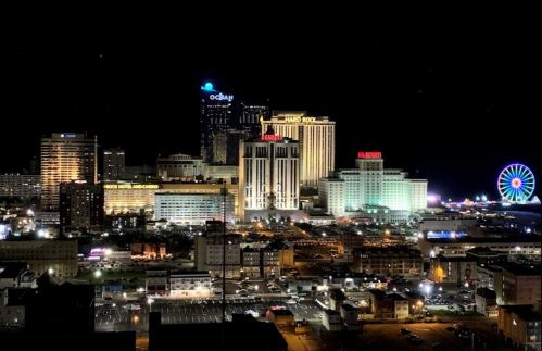 A vibrant night view of Atlantic City, featuring illuminated casinos and a Ferris wheel against a dark sky.
