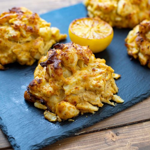 Golden-brown crab cakes on a slate platter, garnished with a halved lemon.