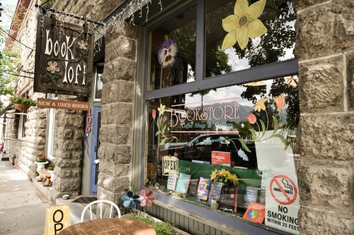 A cozy bookstore with a colorful sign, flowers painted on the window, and a "No Smoking" sign nearby.