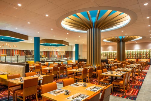 Modern restaurant interior with colorful decor, wooden tables, and stylish lighting fixtures.
