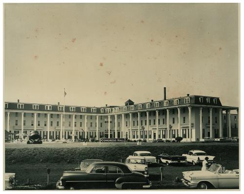 Historic black-and-white photo of Congress Hall, a large building with columns, surrounded by vintage cars.