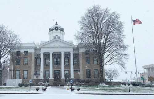 Historic courthouse in snowy weather, with an American flag flying and trees in the foreground.