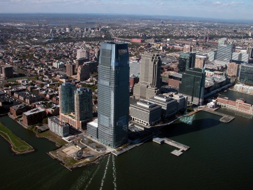 Aerial view of a city skyline featuring modern skyscrapers along a waterfront with a clear blue sky.