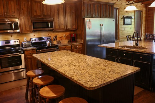 A rustic kitchen with wooden cabinets, granite countertops, stainless steel appliances, and a central island with stools.
