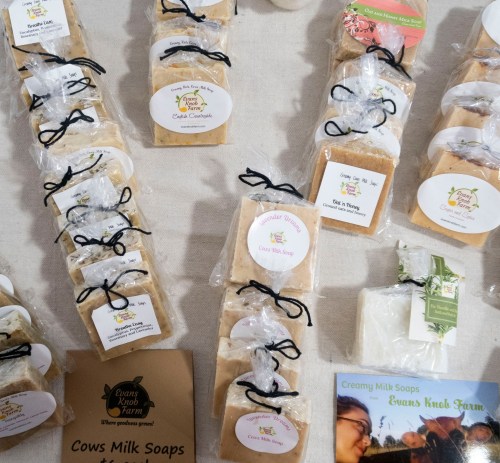 A display of handmade soaps wrapped in clear bags, labeled, and tied with black ribbon on a table.