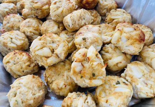 A close-up of golden-brown crab cakes arranged in a tray, showcasing their textured surface and round shape.