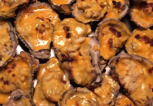 A close-up of baked oysters topped with melted cheese and bits of bacon, arranged on a tray.