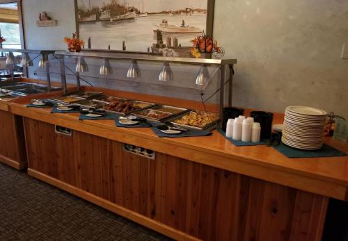 A buffet table with warm food trays, cups, and stacked plates in a cozy dining area with a waterfront view.