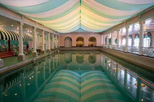 Indoor swimming pool with a colorful ceiling, surrounded by elegant decor and soft lighting.